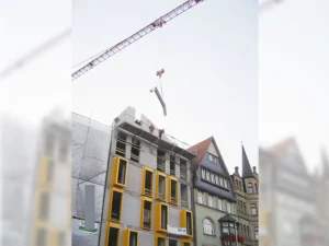 Anbringung einer Dachkonstruktion mit Kran an unfertigem Haus mit gelben Fensterrahmen